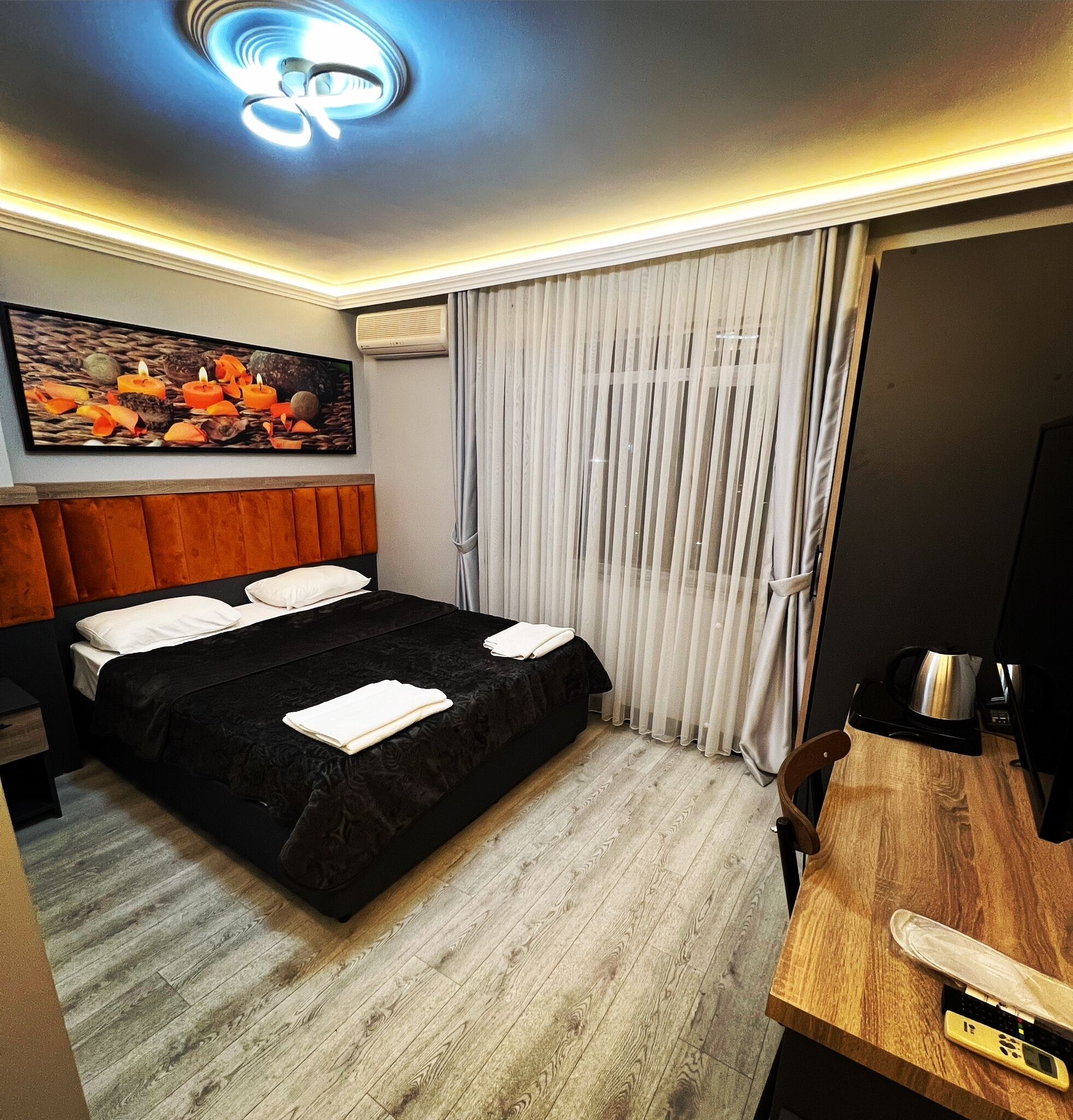 A hotel room with a bed, a wooden desk, a coffee maker, and a painting on the wall.