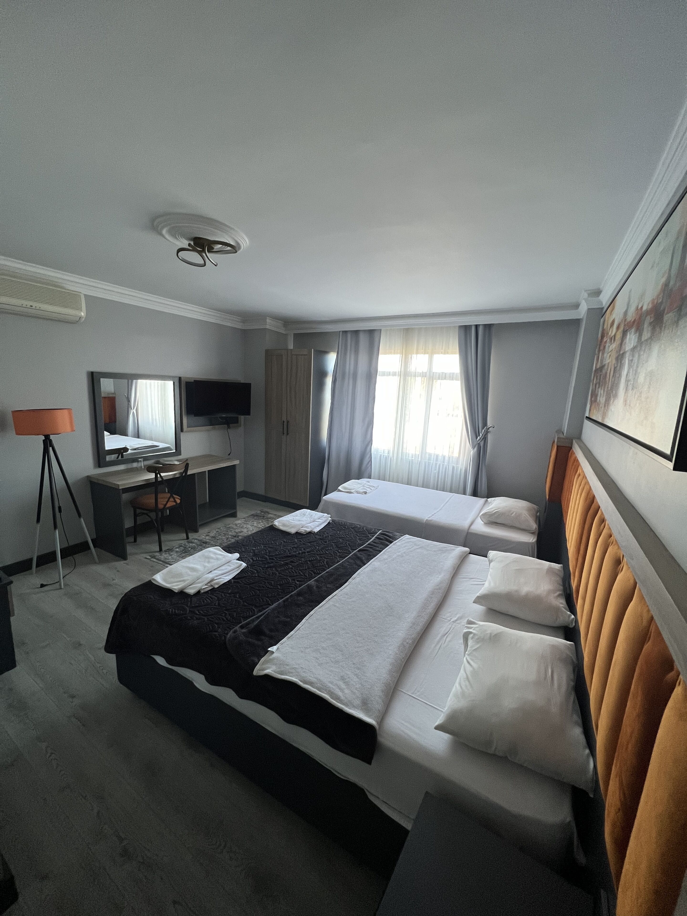 A hotel room with two beds, a desk, a chair, a TV, and a painting on the wall.
