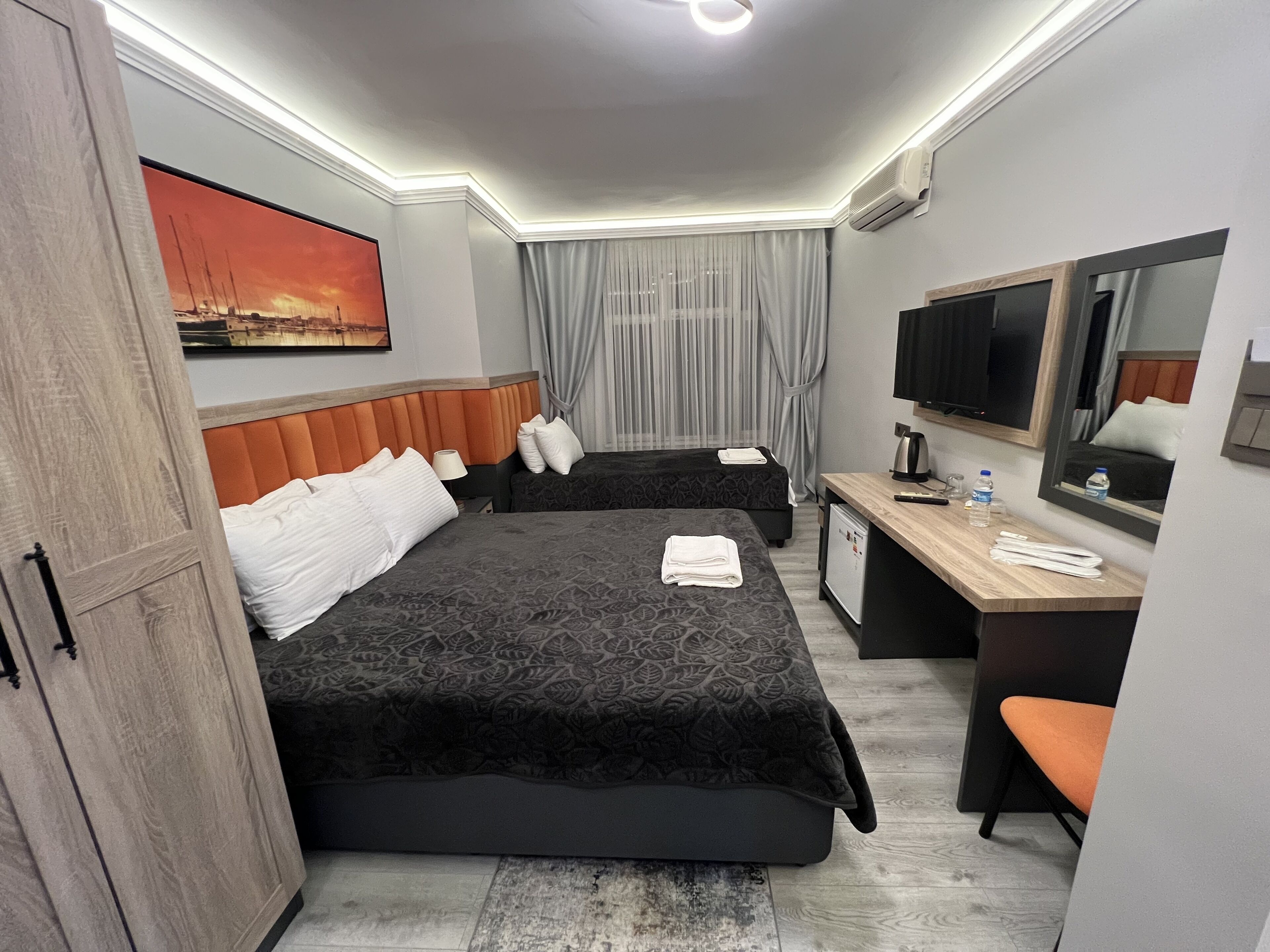A hotel room with two beds, a desk, a chair, a TV, and a window with curtains.
