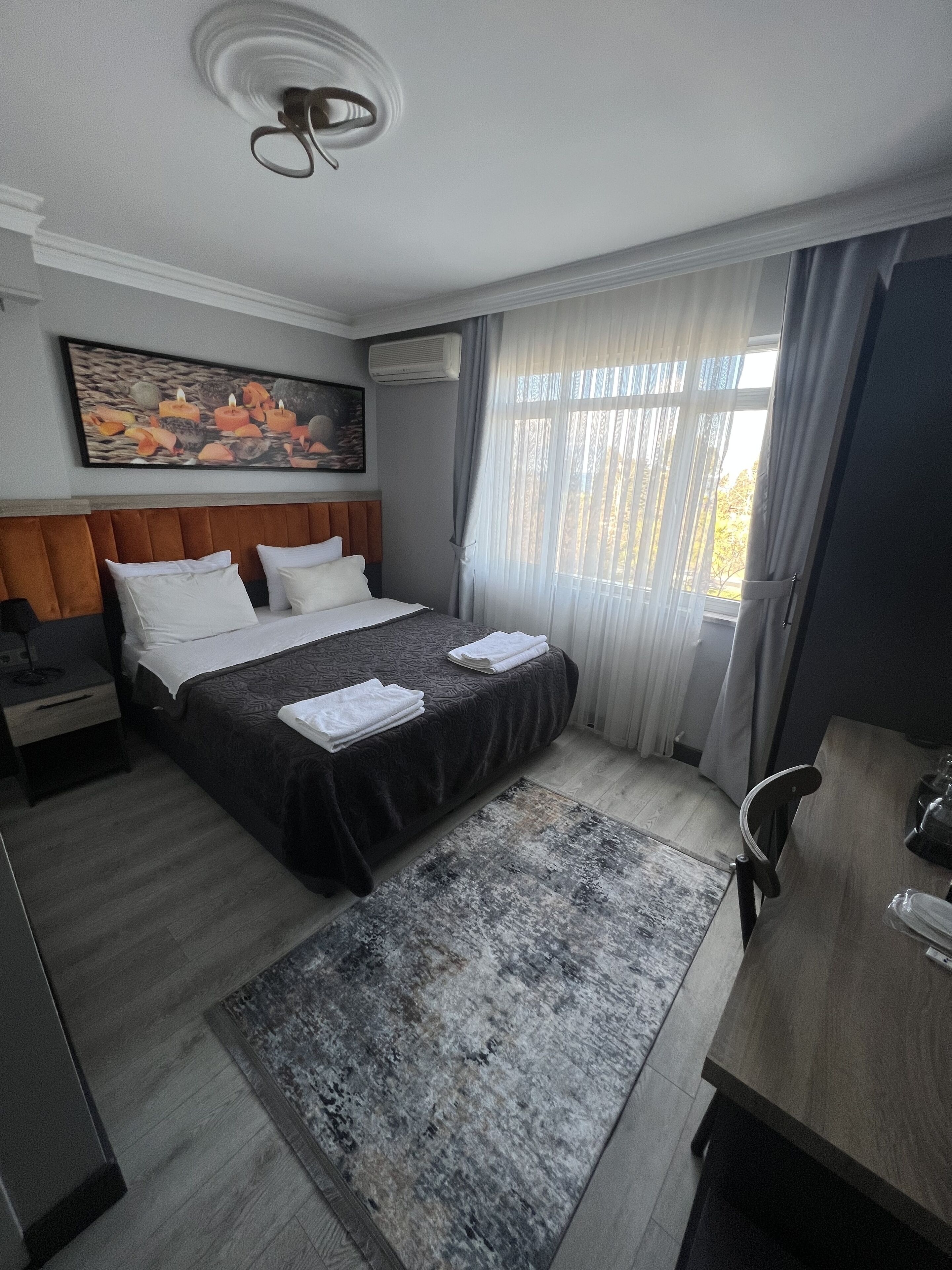 A modern hotel room with a large bed, a desk, and a painting on the wall.