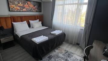 A modern hotel room with a large bed, a desk, and a painting on the wall.