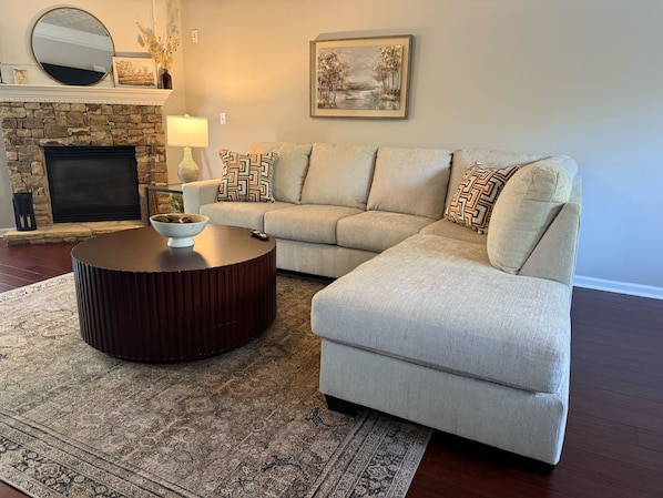 A living room with a stone fireplace, a round coffee table, a beige sofa, and a patterned rug.
