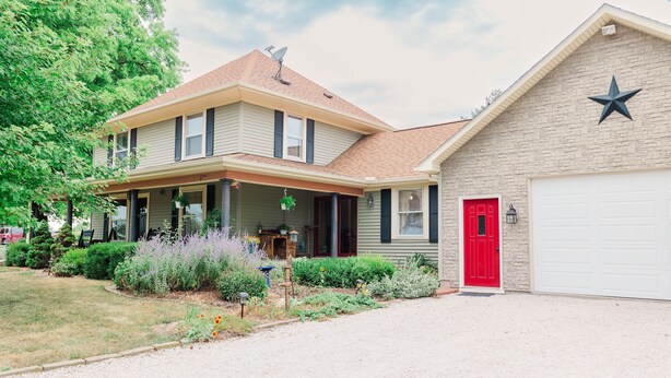 Une maison à deux étages avec un porche à l’avant, une porte de garage rouge et un mur en briques orné d’un emblème en forme d’étoile.