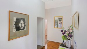 Un couloir orné de tableaux encadrés, avec un lustre et une plante en pot fleurie.