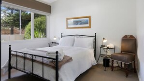 Une chambre à coucher bien rangée, avec un lit, des tables de chevet, une chaise et une fenêtre donnant sur un paysage verdoyant.