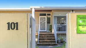 Une maison de ville portant le numéro 101, avec un petit jardin devant et une enseigne publicitaire annonçant un hébergement de qualité.