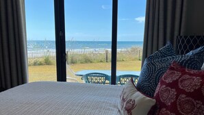 A bedroom with a large bed, a view of the beach, and a balcony with chairs. - Beautiful Ground Floor with a Panoramic View of the Gulf of Mexico (Orange Beach)