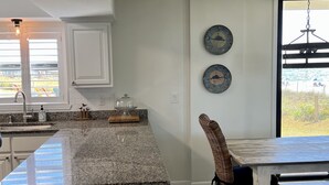 A kitchen with a granite countertop, white cabinetry, and a dining area with a table and chairs. - Beautiful Ground Floor with a Panoramic View of the Gulf of Mexico (Orange Beach)