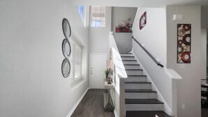 Una escalera con barandilla, una puerta al final y un muro con espejos decorativos y una obra de arte circular.