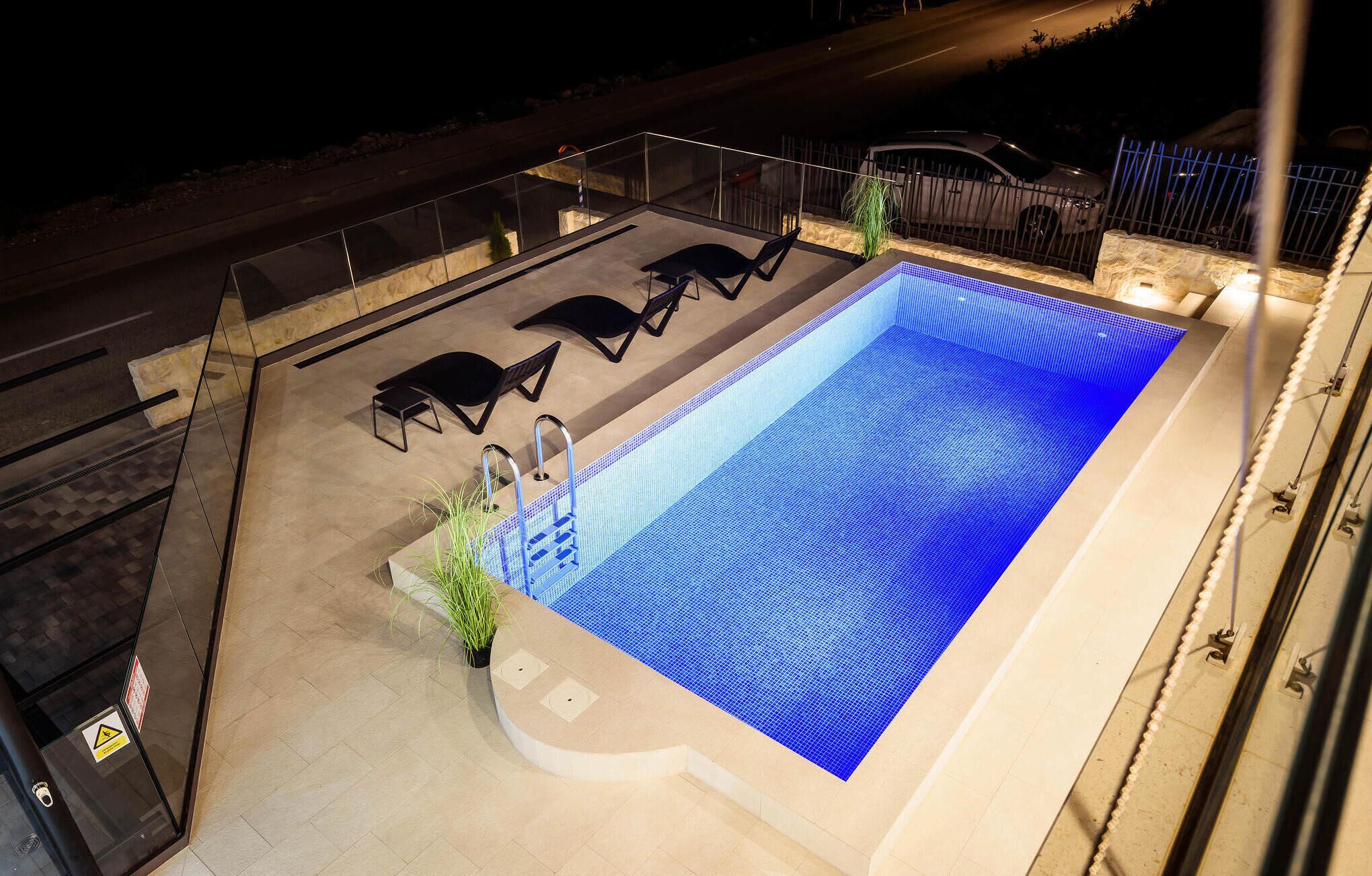 Une piscine sur le toit, avec un sol carrelé de bleu, entourée de chaises longues et protégée par une rambarde en verre.