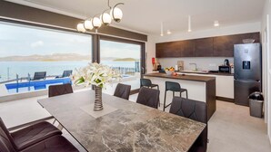 A modern kitchen with a view of the sea, a dining area with a marble table, and a kitchen island with a sink and appliances. - Awesome home in Drace with sauna (Drace)