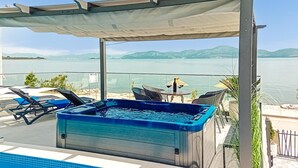 A hot tub with a view of a lake and mountains, surrounded by lounge chairs and a table with drinks. - Awesome home in Drace with sauna (Drace)