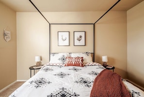 Een slaapkamer met een bed, twee nachtkastjes, een wandlamp en twee ingelijste foto’s.