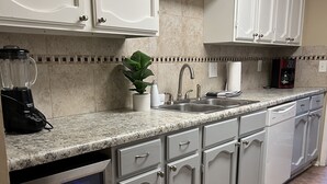 Eine Küche mit weißen Schränken, einer Granitarbeitsplatte, einem eingebauten Geschirrspüler und einer Kaffeemaschine.