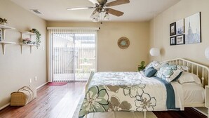 Ein Schlafzimmer mit einem Bett, einem Deckenventilator, einem Fenster mit Jalousien und einer Wand mit gerahmten Bildern.