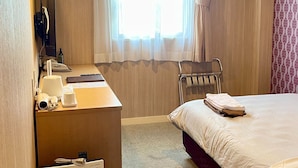 Una habitación de hotel con cama, escritorio con computadora, silla y ventana con cortinas.
