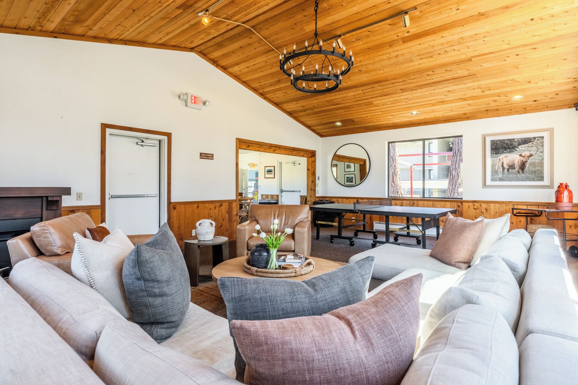 A cozy living room with a wooden ceiling, a round mirror, a billiards table, and a sofa with cushions.