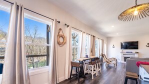 A spacious room with large windows, a wooden dining table, and a television.