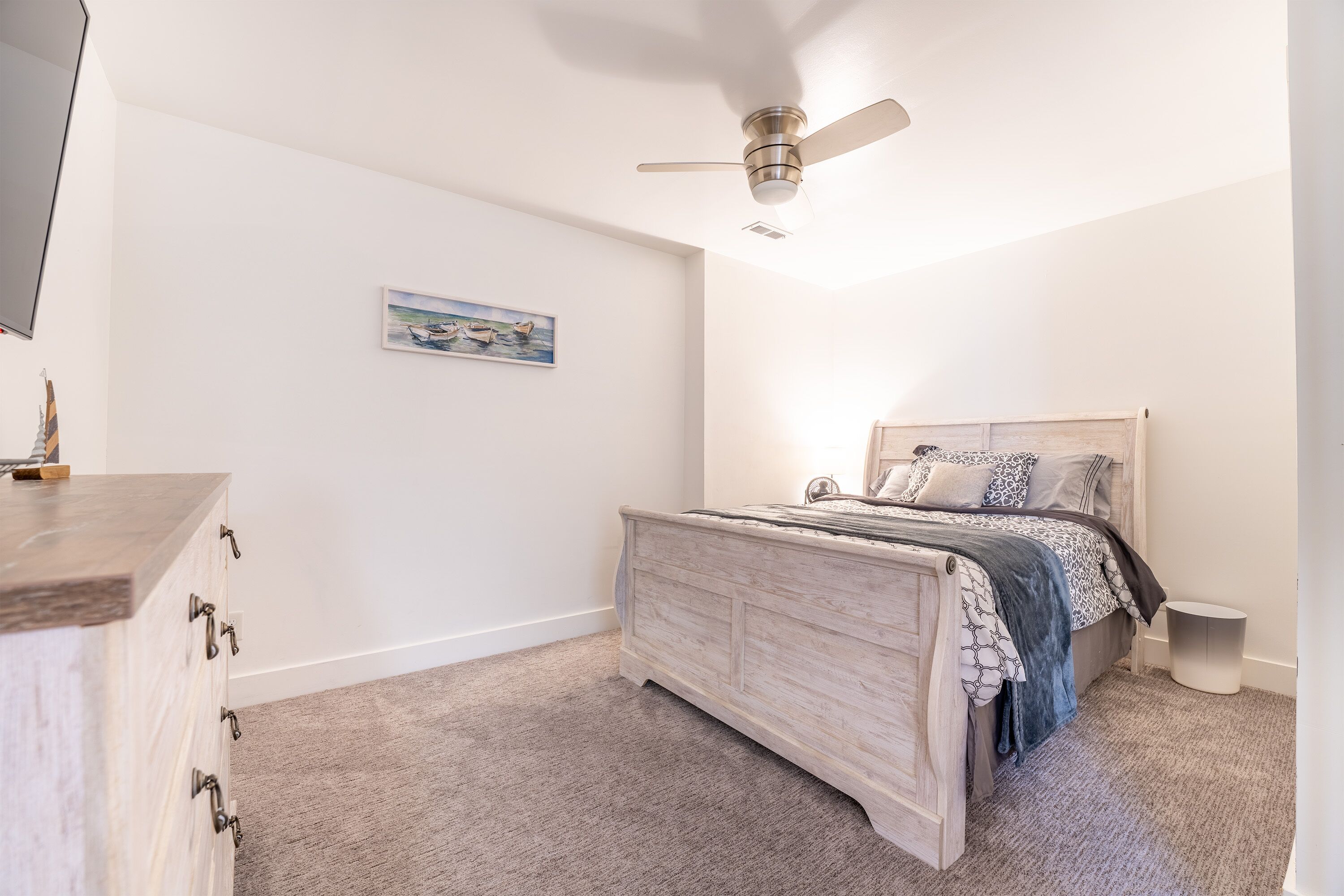 Quarto com cama de madeira, ventoinha no teto, mesa de cabeceira e criado-mudo redondo.