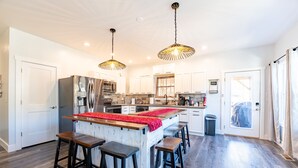 A modern kitchen with a central island, bar stools, hanging pendant lights, and a view of the adjacent living area.