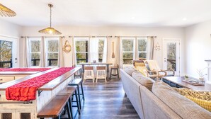 A spacious room with a wooden dining table, benches, a sofa, and a large window with curtains.