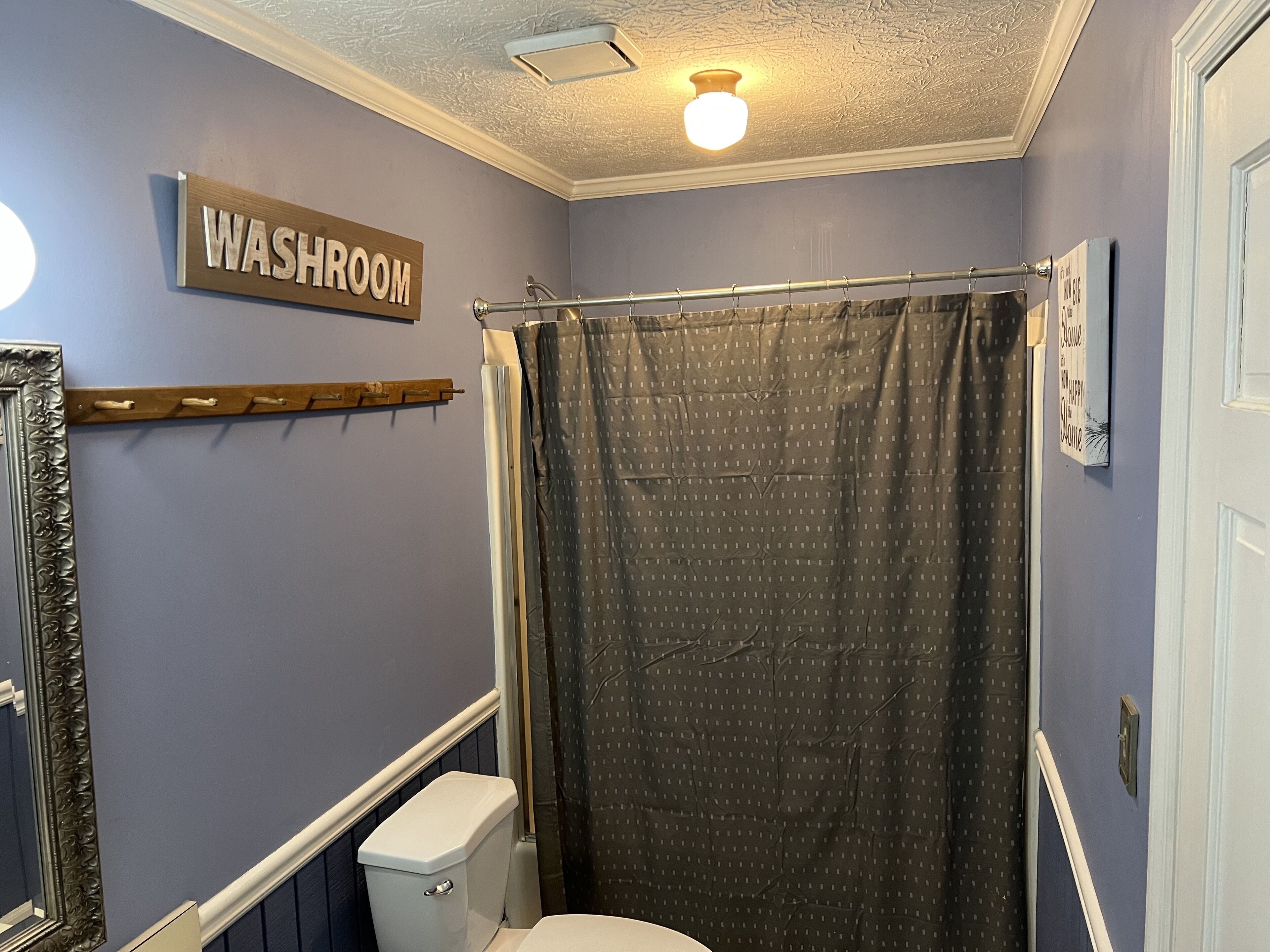 Une salle de bain équipée de toilettes, d’un rideau de douche, d’une pancarte indiquant « TOILETTES », d’un miroir et d’un luminaire.