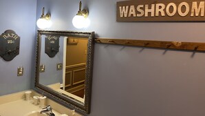 Une salle de bain avec un grand miroir, un lavabo et une pancarte indiquant « TOILETTES » sur le mur.