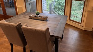 Un coin repas avec une table en bois, des chaises et une mangeoire à oiseaux placée à l’extérieur, près de la fenêtre.