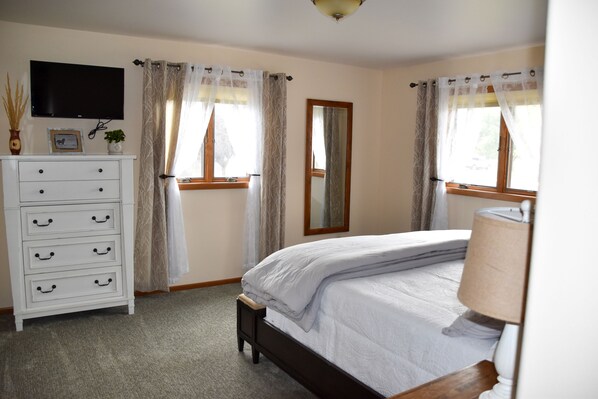 A bedroom with a bed, a dresser, a TV mounted on the wall, and a window with curtains. - Beautiful Spacious Home - Near Fergus High School (Lewistown)