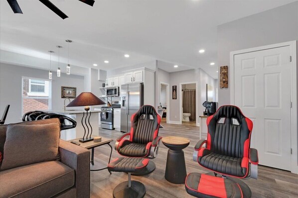 A modern living room with a sofa, two gaming chairs, a coffee table, and a lamp.