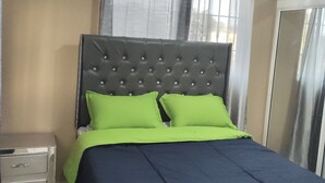 Una cama bien tendida con un cabecero capitonado, una mesita de noche y una ventana con cortinas.