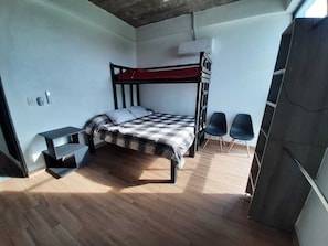 A bunk bed with a checkered blanket, a small table, two chairs, and a wardrobe.