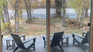 A deck with Adirondack chairs overlooking a river and a forest. - Stillwater Riverfront Home, Close to the Beartooths, Fish from your door - Peace (Absarokee)
