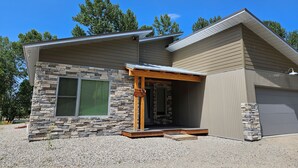 A modern house with a stone facade, a covered porch, and a garage. - Stillwater Riverfront Home, Close to the Beartooths, Fish from your door - Peace (Absarokee)