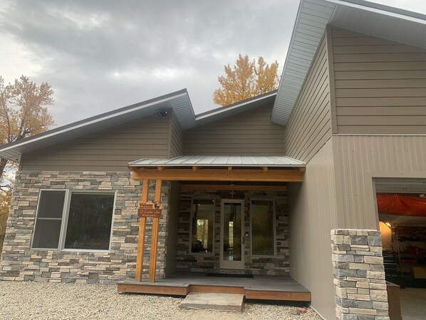 A modern house with a stone facade, a wooden porch, and a garage. - Stillwater Riverfront Home, Close to the Beartooths, Fish from your door - Peace (Absarokee)