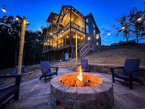Relax by the fire pit on the patio, surrounded by trees and a grassy hill.