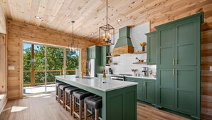 Een moderne keuken met een groot eiland, groene kastjes en een houten plafond.