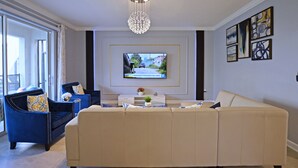 Un salon moderne avec un canapé beige, un fauteuil bleu et un téléviseur fixé au mur.