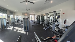 Une salle de sport équipée de divers appareils d’exercice, de ventilateurs de plafond et d’un grand miroir.