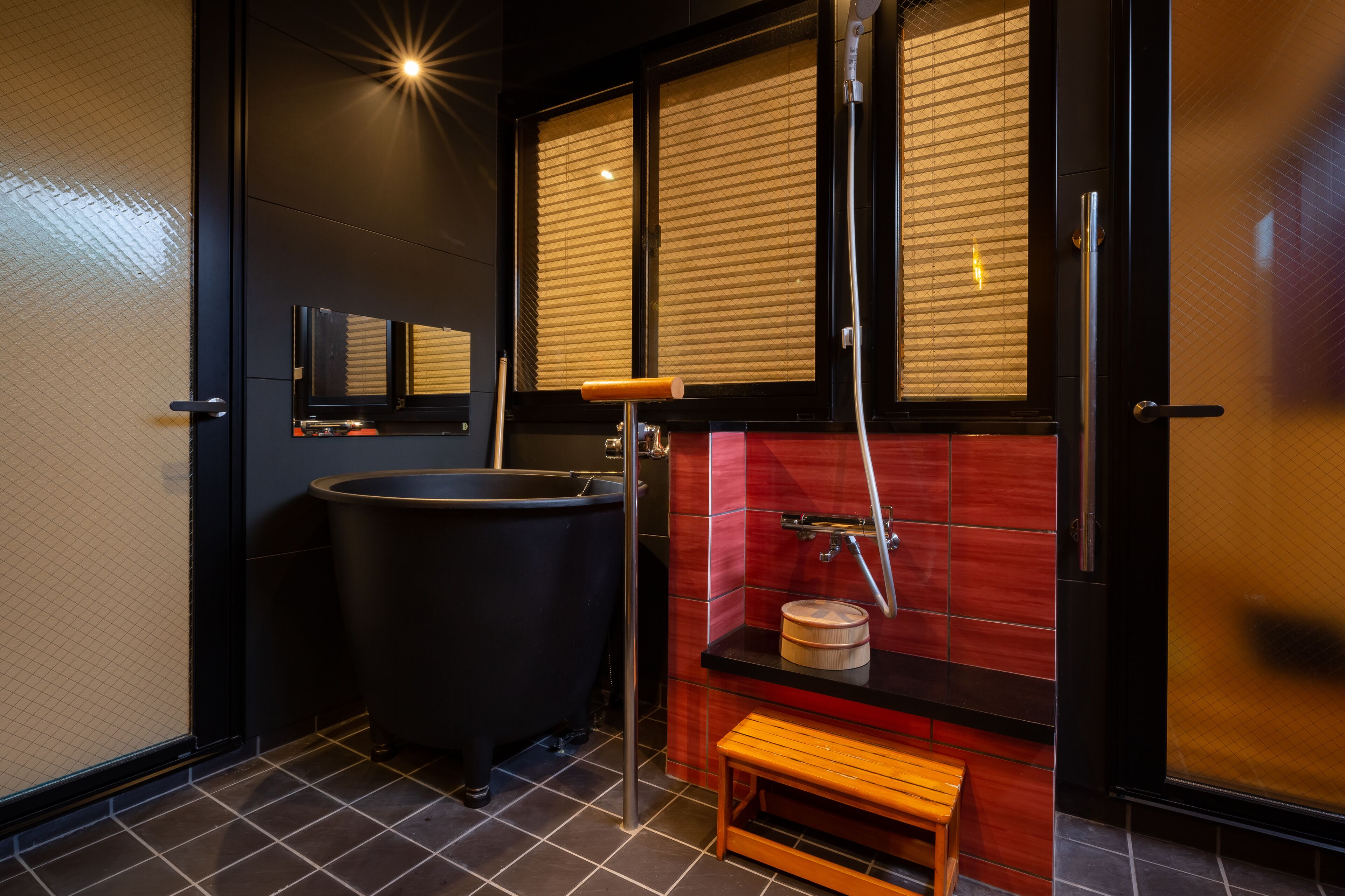 A modern bathroom with a black bathtub, a wooden bench, and a red tiled wall.