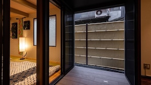 A traditional Japanese room with tatami flooring, a shoji screen door, and a sliding glass door leading to a balcony. - TSUDOYA Sannou (Osaka)