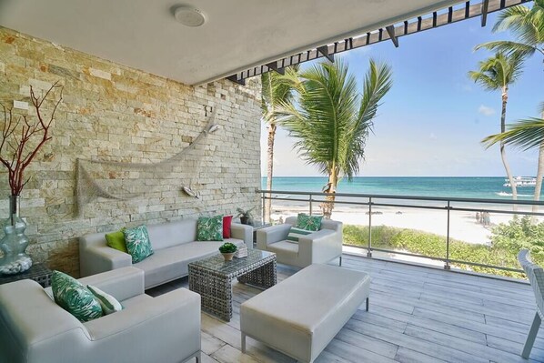 A balcony with a view of the beach, white sofas, and a stone wall.