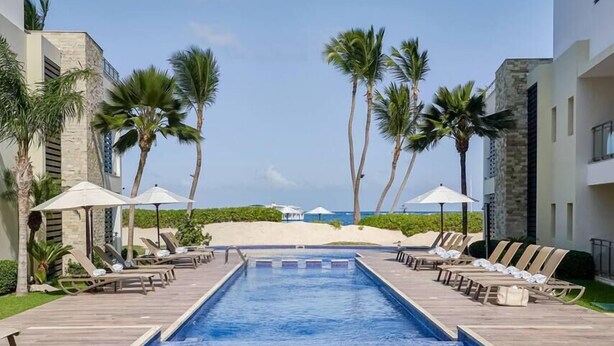 Una piscina con tumbonas y sombrillas, palmeras y vista al mar.