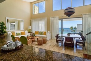 A spacious living area with a dining table, chairs, a sofa, and a large window overlooking the ocean.
