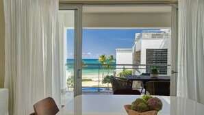 Un balcón con vistas a la playa y al océano, una mesa con sillas y un cuenco de fruta.