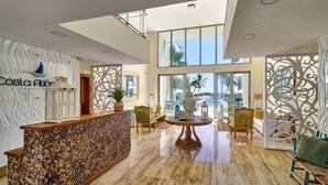 Un hall con mostrador de recepción, zona de estar y amplias ventanas con vistas al exterior.