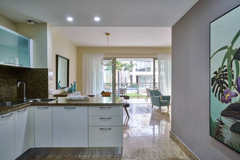 Een moderne keuken met een centraal eiland, een eethoek met tafel en stoelen, en een groot raam met gordijnen.
