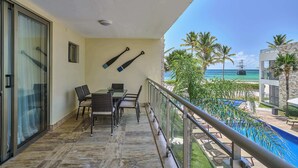 Un balcon avec une table et des chaises, une porte vitrée et une vue sur la piscine et la plage.
