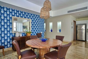 A dining area with a round wooden table, brown leather chairs, a blue bowl, and a pineapple-patterned wallpaper.