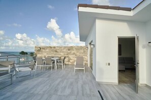 A modern outdoor patio with a view of the sea, a stone wall, and a white building with a door leading to an interior room. - Beach Penthouse Sea View Bh-401 @Costa Atlantica (Punta Cana)